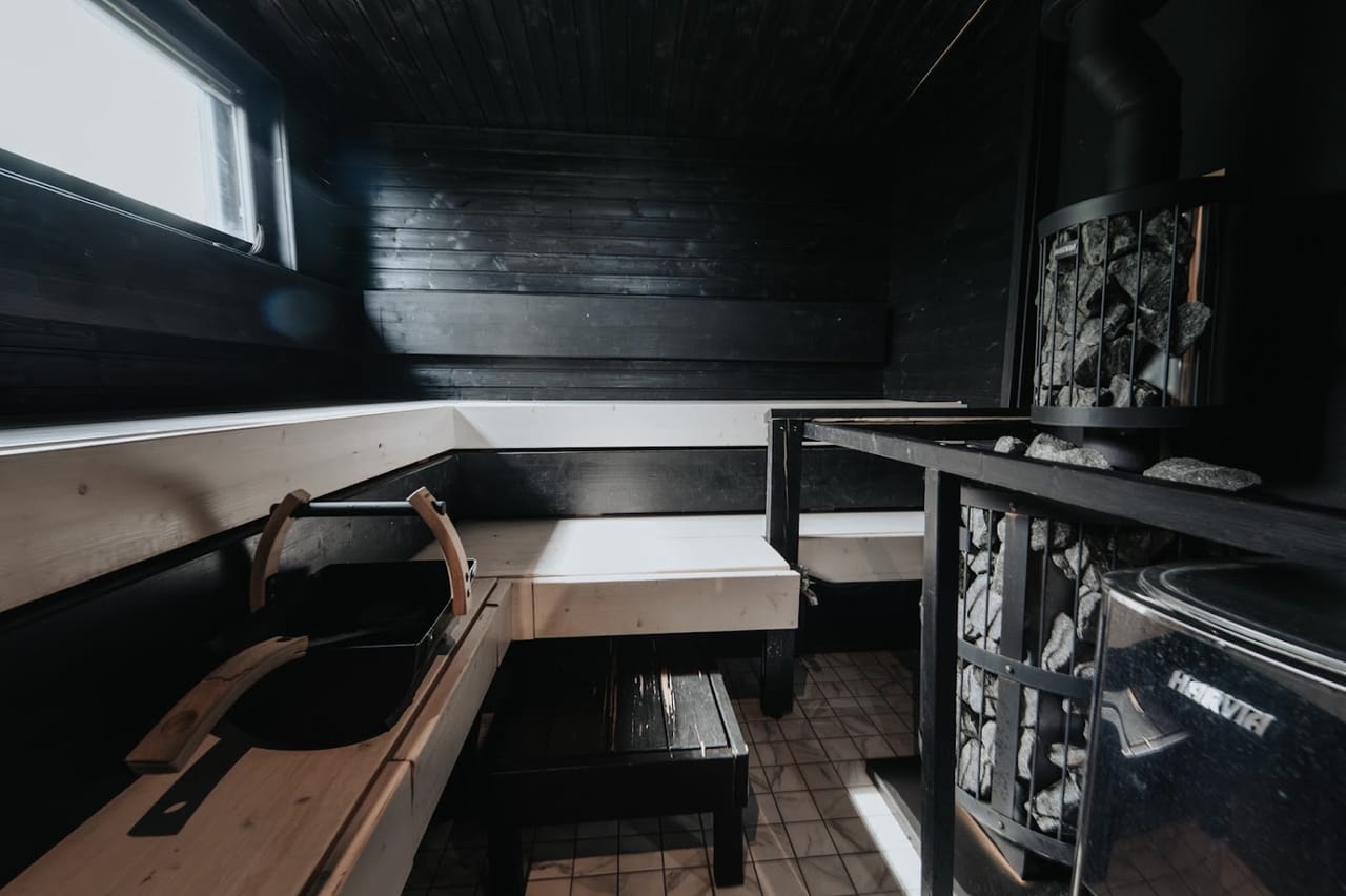 Puulämmitteinen sauna ulkorakennuksessa, kiuas ja vaaleat lauteet